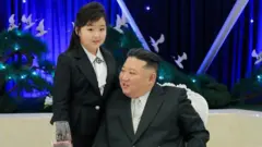 Com os longos cabelos presos, Kim Ju Ae está ao lado de Kim Jong Un, sentado em uma cadeira branca, ambos vestindo ternos pretos e camisas brancas de colarinho combinando. Na gola, ela usa um broche verde estampado, enquanto ele usa uma gravata clara. Um fundo azul-escuro apresenta árvores em miniatura, pássaros brancos em voo e luzes. Uma taça de vinho está em primeiro plano.