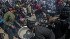 نازحون فلسطينيون يجمعون التبرعات الغذائية في جباليا، شمال غزة - 2 مايو/أيار 2025