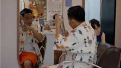 Un hombre frente a un espejo rociándose algo en su cabello con un espray