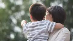 設計圖片：一位日本母親（右）背對鏡頭，抱著年幼小孩；小孩舉起左手指向前方