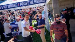 Charlie Kirk izdiham arasında, əlində "Make America Great Again" papaqları.