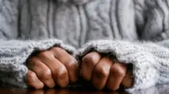 Foto de banco de imagem mostra as mãos de mulher fechadas em cima de uma mesa de madeira