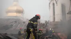 Пошкоджений дах церкви: на передньому плані кілька рятувальників у захисному одязі та шоломах працюють серед уламків і згорілих конструкцій. Навколо багато диму, який частково затягує куполи.