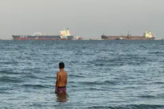 Un hombre entra en el agua con el buque petrolero Ionic Anax y el buque cisterna para petróleo y productos químicos Stef atracados al fondo, en el lago de Maracaibo, en Maracaibo, Venezuela, el 1 de marzo de 2026. Venezuela fue en el pasado un importante proveedor de crudo para EE.UU. y posee las mayores reservas probadas del mundo, con más de 303.000 millones de barriles, según el cartel petrolero mundial de la OPEP. (Foto de Margioni BERMÚDEZ / AFP vía Getty Images)