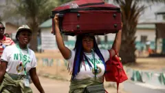 Aworan awọn Agunbanirọ obinrin meji, ọkan ru baagi rẹ sori, o gbe baagi keji kọ apa. Agunbanirọ obinrin kan naa n rin bọ leyin rẹ 