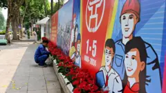 Aworan oṣiṣẹ to n gbin ododo niwaaju patako ikede ọjọ awọn oṣiṣẹ