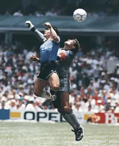 Diego Maradona, da Argentina, usa a mão para marcar o primeiro gol de sua equipe durante uma partida das quartas de final da Copa do Mundo FIFA de 1986 entre Argentina e Inglaterra, no Estádio Azteca, em 22 de junho de 1986. Maradona afirmou posteriormente que o gol foi marcado pela "Mão de Deus".