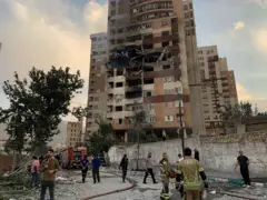 Prédio destruído, com bombeiros e repórter em volta