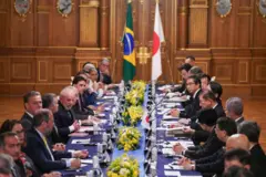 Mesa de reunião com integrantes dos governos brasileiro e japonês. Bandeiras do Brasil e do Japão ao fundo.