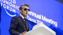 Macron falando em um microfone. Ele usa terno e óculos escuros