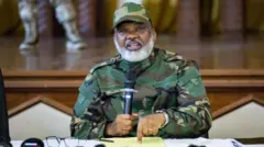 Corneille Nangaa yambaye imyenda ya gisirikare afite microphone arimo kuvuga