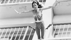 Una imagen en blanco y negro de Kitty O'Neil saltando con los brazos extendidos desde el balcón de un hotel disfrazada de Mujer Maravilla