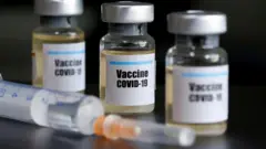 "Вакцина Covid-19" деген жазуусу бар кичнинекей айнек идиш