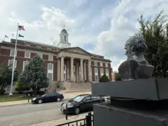 El busto de Artigas visto de atrás, y enfrente el ayuntamiento de Elizabeth.