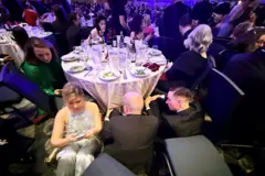 Personas vestidas con trajes de gala sentadas en el piso del evento.