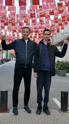Dva muškarca stoje ispred zastava Crne Gore i prstima pokazuju slovo L.