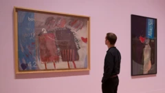 Pracownik pozuje obok dzieł zatytułowanych: „We Two Boys Together Clinging, 1961” (po lewej), „The Most Beautiful Boy in the World, 1961” (w centrum) oraz „Tea Painting in an Illusionistic Style, 1961”, autorstwa brytyjskiego artysty Davida Hockneya, podczas fotocallu promującego retrospektywę jego twórczości w Tate Britain w Londynie, 6 lutego 2017 roku.