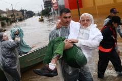 Voluntário carrega idoso resgatado em área de enchente em Porto Alegre