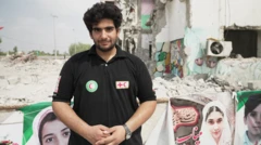 Reza Besharati, rescatista de la Media Luna Roja, aparece en la foto con una camiseta negra con insignias de la organización. Está de pie frente a pancartas que muestran los rostros de las personas fallecidas en el ataque a la escuela, con los edificios dañados a sus espaldas.