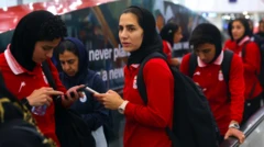 İran kadın milli futbol takımının oyuncuları endişeli şekilde telefonlarına bakıyor. Hepsi kırmızı giymiş ve havalimanı yürüyen merdivenindeler.