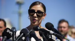 Mulher falando ao ar livre, cercada por microfones e pessoas