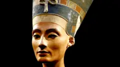 Uma escultura da cabeça da rainha egípcia Nefertiti sobre fundo preto, mostrando o delineador preto nos olhos