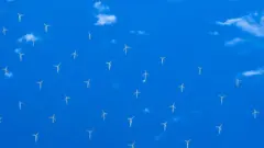 Grupo de turbinas eólicas no mar visto de cima, com o céu refletido na superfície