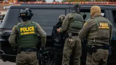 Agentes de inmigración rodean a un presunto inmigrante indocumentado que está colocado junto a un vehículo. La foto fue tomada en Illionis en octubre de 2025.