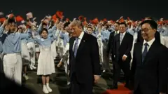 ダークスーツ姿のトランプ氏が米中の国旗を振る人たちの歓迎を受けながら赤じゅうたんの上を歩いている。近くには出迎えの中国高官らがいる