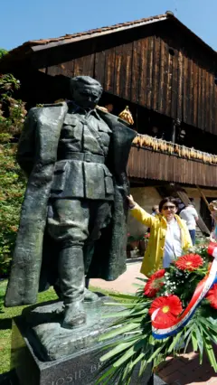 statua josipa broza tita u kumrovecu i zena koja stoji pored njega sa cvecem