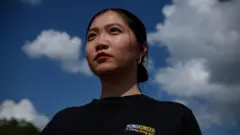 郭凤仪望向前方，身穿黑色T恤，头发紮成发髻，身后是蓝天白云。