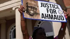 A demonstrator holds a sign at the Glynn County Courthouse as jury selection begins in the trial of the shooting death of Ahmaud Arbery