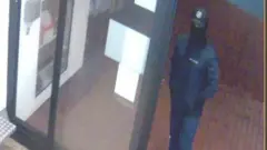 Imagem mostram homem encapuzado com as mãos no bolso