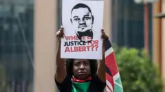 Uwigaragambya witeye ibendera rya Kenya afite icyapa kiriho ifoto ya Albert Ojwang iherekejwe n'amagambo yo mu Cyongereza agira ati: "Ubutabera kuri Albert buri hehe?"
