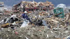 Un policía con casco y equipo protector sube a una montaña de escombros que incluyen autos destrozados