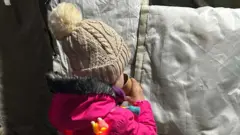 Дитина у рожевому комбінезоні і бежевій шапці п'є чай у пункті незламності 