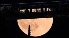 Pessoas no topo do Shanghai World Financial Centre, na China, que lembra uma ponte, enquanto a gigante Lua de Sangue se ergue acima dos arranha-céus no distrito financeiro.