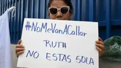 Uma mulher protesta contra a prisão da advogada de direitos humanos Ruth López, com um cartaz em que se lê: Ruth não está sozinha, do lado de fora do centro judicial Isidro Menéndez em San Salvador, em 4 de junho de 2025