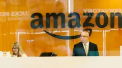 Une femme assise devant ce qui semble être un ordinateur et un homme debout, dans un bureau d'Amazon. 