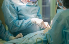 Médicos vestidos de azul, con mascarillas y con guantes blancos en un pabellón realizando una operación