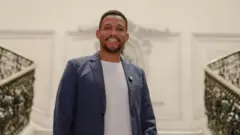 Rick Azevedo sorrindo e olhando para a câmera em uma escadaria imponente na Câmara dos Vereadores do Rio de Janeiro