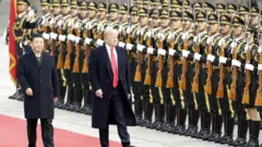 Xi Jinping e Donald Trump passam por tropas chinesas vestidas de branco e segurando armas. Tanto Xi quanto Trump usam ternos escuros.