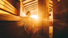 Kobieta relaksuje się w saunie, przez okno wpadają promienie słońca
