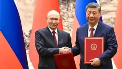Putin ve Şi imzaladıkları anlaşmaları ellerinde tutuyor ve tokalaşıyorlar