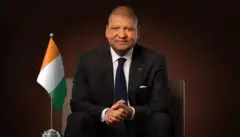 Jean Louis Billon, en costume sombre, cravatte bleue, avec le drapeau ivoirien posé à sa droite