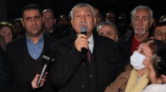 Zeydan Karalar elinde mikrofonla konuşuyor. Yanında birçok kişi var. Bir kadın maskeli şekilde ona bakıyor.