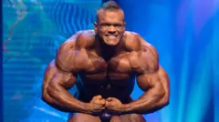 Dallas McCarver sur scène à l'Arnold Classic, posant devant un fond bleu et exhibant sa musculature imposante.