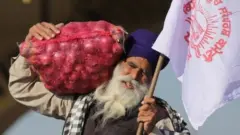 A farmer carries a bag of onions and a flag prior to the start of a march towards New Delhi to protest against new farm laws, on the outskirts of Amritsar, India, 27 November 2020.