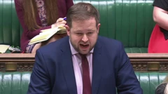 イギリス下院で答弁するダウティー氏。ダークスーツにピンクのシャツ、赤いネクタイをしている