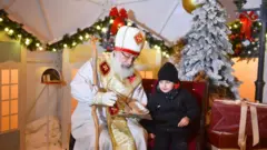 Чоловік у костюмі Святого Миколая спілкується із хлопчиком. Резиденція Миколая у новорічних прикрасах. 